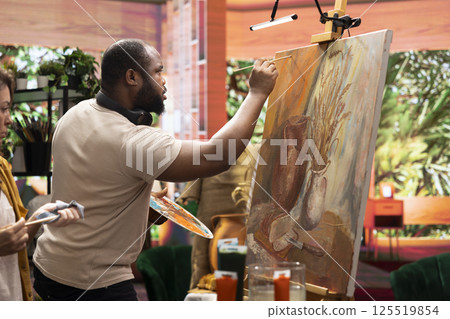 Team of skilled artist collaborating on a rustic painting in art studio, using creative painting techniques with brushes and watercolor paint. Applying multicolored dye with careful brushstrokes. 125519854