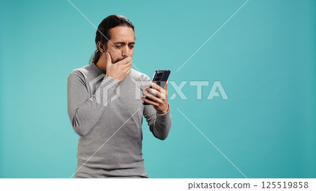 Man holding mobile phone, browsing betting website, celebrating after winning money, isolated over studio background. Cheerful person feeling happy while scrolling on smartphone, camera B 125519858