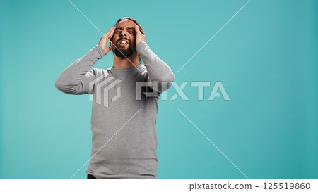 Portrait of man feeling exhausted from overworking, suffering from headache, isolated over studio background. Tired person feeling pain from fatigue, studio backdrop, camera B 125519860