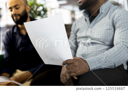 Diverse team of office clerks looking over revenue figures on documents in office. Multiethnic staff members comparing company statistical numbers, working hard to finish job before deadline Diverse team of office clerks looking over revenue figures on documents in office. Multiethnic staff members comparing company statistical numbers, working hard to finish job before deadline 125519887
