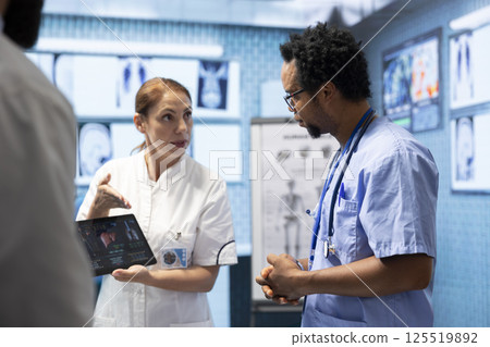 Doctors discuss x ray and ct scan results for a new treatment plan in a medical office. Team of licensed experts working to provide diagnostic and healthcare services, examine organs radiography. Doctors discuss x ray and ct scan results for a new treatment plan in a medical office. Team of licensed experts working to provide diagnostic and healthcare services, examine organs radiography. 125519892