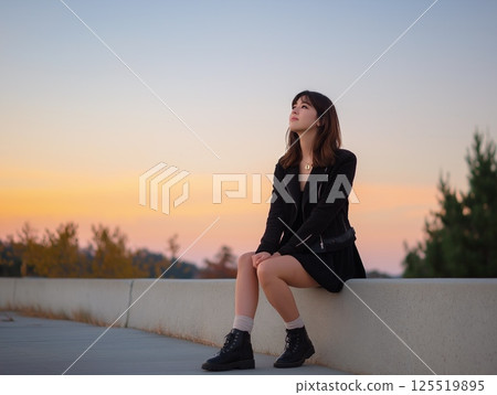 日落時分，一位女士坐在人行道上，仰望天空 125519895