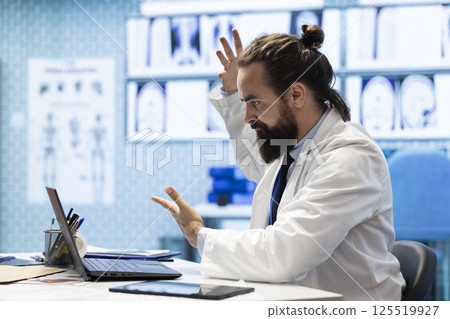 Worried stressed doctor working under pressure for disease prevention, analyzing radiography results and healthcare records. Physician searching for the right treatment plan, medical facility. 125519927