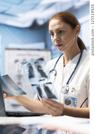 General practitioner examining x ray scans test results to find the right treatment in private clinic, medical specialist looking at radiography for a diagnostic. Woman physician working at facility. General practitioner examining x ray scans test results to find the right treatment in private clinic, medical specialist looking at radiography for a diagnostic. Woman physician working at facility. 125519928