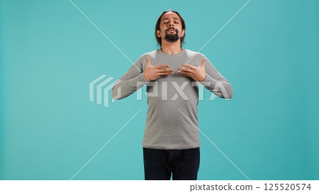 Portrait of man inhaling and exhaling to relax and gain positive energy, eliminating stress. Person doing breathing exercises for wellbeing, isolated over studio background, camera A 125520574