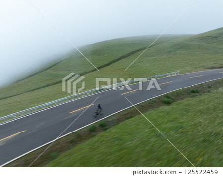 Motion blurred cyclist riding bike on grassland mountain top trail 125522459