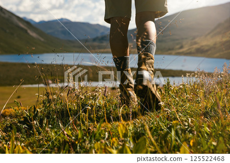 Hiker legs wearing leather boots hiking on high altitude mountain top,with a lake in the distance Hiker legs wearing leather boots hiking on high altitude mountain top,with a lake in the distance 125522468