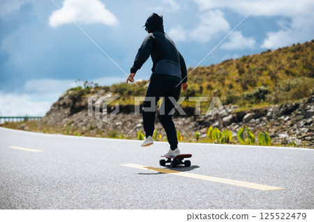 Skateboarder skateboarding on the mountain road Skateboarder skateboarding on the mountain road 125522479