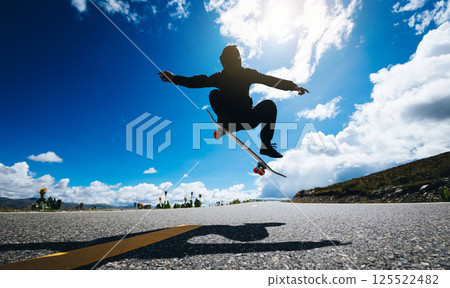 Skateboarder skateboarding on country road 125522482