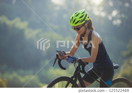 Woman cyclist using mobile phone in summer park Woman cyclist using mobile phone in summer park 125522489