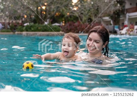 Caucasian woman holds son while swimming in pool on vacation. Caucasian woman holds son while swimming in pool on vacation. 125523262