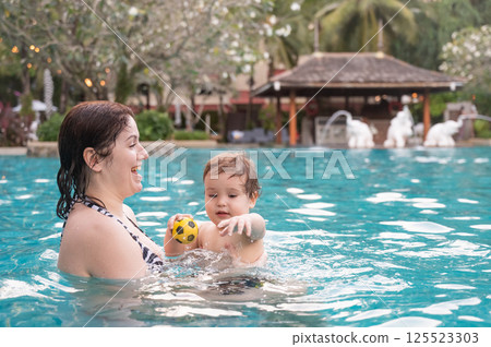 Caucasian woman holds son while swimming in pool on vacation. Caucasian woman holds son while swimming in pool on vacation. 125523303
