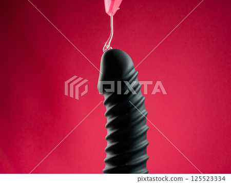 Lube pouring on black dildo on pink background. Lube pouring on black dildo on pink background. 125523334