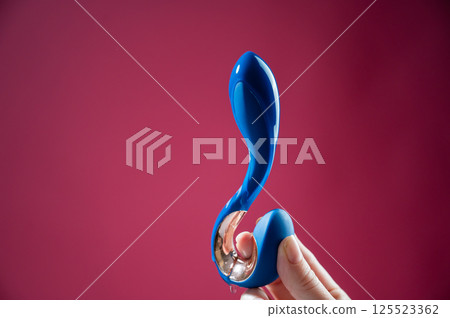 Lube pouring onto blue sex toy on pink background.  125523362
