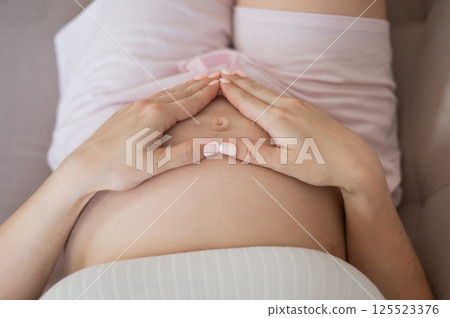 Pregnant woman holds her hands in a heart shape on her belly.  125523376