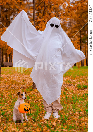 Woman in white sheet and jack russell terrier dog holding jack o latrine in autumn forest. Halloween costume. Vertical photo. Woman in white sheet and jack russell terrier dog holding jack o latrine in autumn forest. Halloween costume. Vertical photo. 125523384
