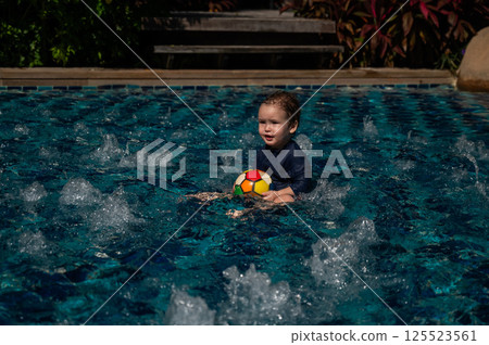 Caucasian one year old boy playing ball in swimming pool. Caucasian one year old boy playing ball in swimming pool. 125523561