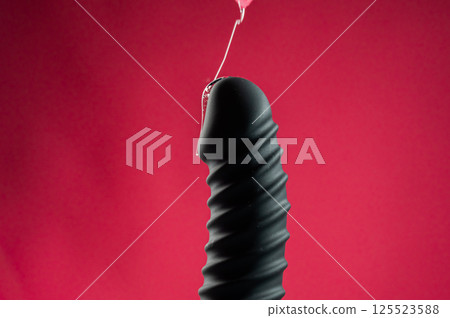 Lube pouring on black dildo on pink background.  125523588