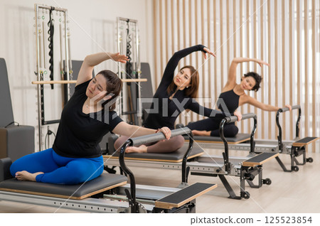 Three Asian women doing Pilates on a reformer. Three Asian women doing Pilates on a reformer. 125523854