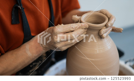 Close-up of a potter's hands making a ceramic vase on a potter's wheel. Close-up of a potter's hands making a ceramic vase on a potter's wheel. 125523993