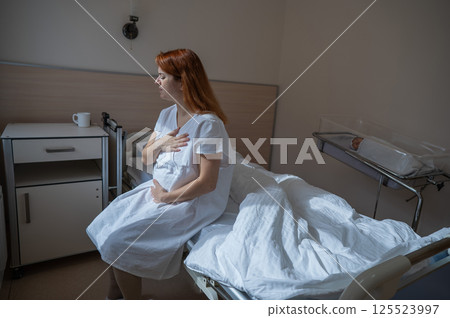 An unhappy woman sits on a couch and holds her stomach in a hospital room after giving birth. An unhappy woman sits on a couch and holds her stomach in a hospital room after giving birth. 125523997