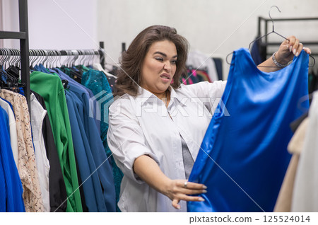A fat woman chooses clothes in a plus size store.  125524014