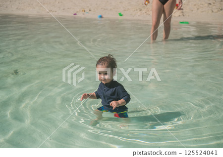 A one-year-old Caucasian boy swims in a pool with a sandy bottom.  125524041