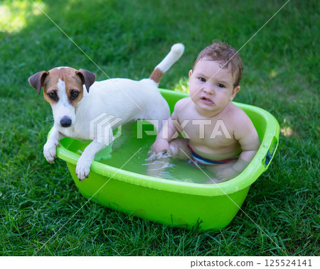 Cute boy bathes in a basin with a Jack Russell terrier dog outdoors in the summer. Cute boy bathes in a basin with a Jack Russell terrier dog outdoors in the summer. 125524141