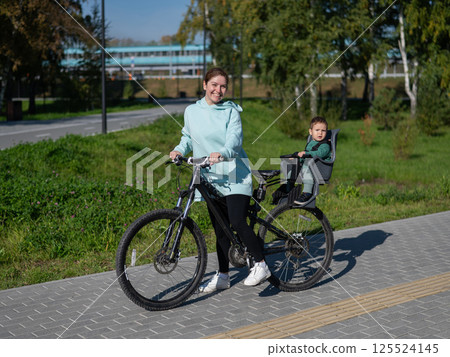 Caucasian woman riding a bicycle with her toddler son sitting behind her in a child seat.  125524145