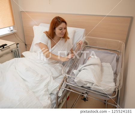 A young mother admires her newborn son in the maternity hospital.  125524181