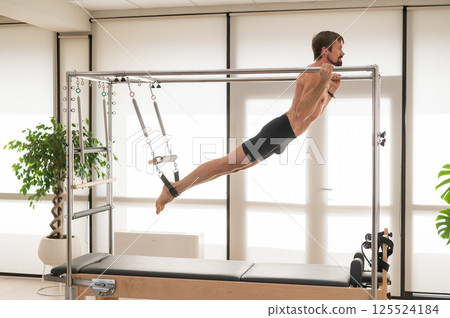 A man performs aerial exercises on a reformer machine. A man performs aerial exercises on a reformer machine. 125524184