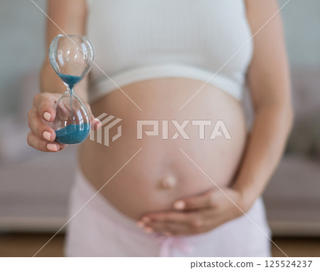 Close up of pregnant woman's belly holding hourglass. Close up of pregnant woman's belly holding hourglass. 125524237