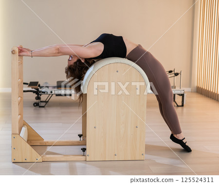 Asian woman exercising on pilates barrel. Asian woman exercising on pilates barrel. 125524311