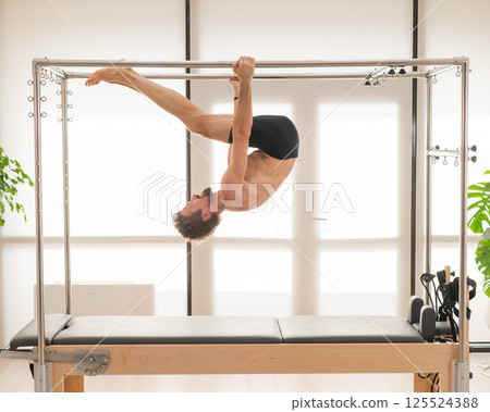 A man performs aerial exercises on a reformer machine. 125524388