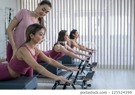A trainer adjusts women on a reformer. A trainer adjusts women on a reformer. 125524399