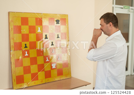 Caucasian man standing at wall mounted magnetic chessboard demonstration.  125524428