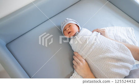 Woman swaddling newborn baby boy on changing table.  125524432