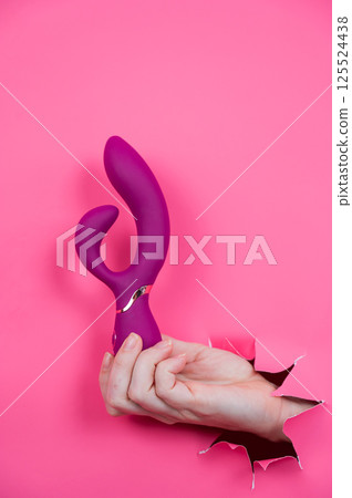 Female hand sticking out with raspberry sex toy from pink paper background. Female hand sticking out with raspberry sex toy from pink paper background. 125524438