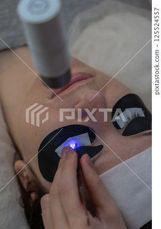 A woman undergoing eyelash extension procedure using an ultraviolet lamp. A woman undergoing eyelash extension procedure using an ultraviolet lamp. 125524557