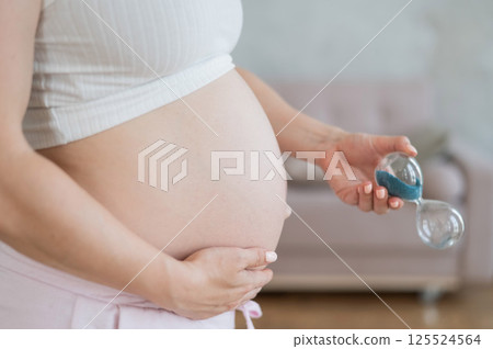 Close up of pregnant woman's belly holding hourglass. Close up of pregnant woman's belly holding hourglass. 125524564
