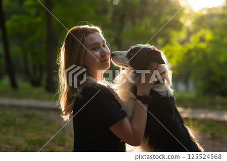 Young Caucasian woman hugging her border collie dog while walking in the park.  125524568