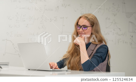 Caucasian woman scientist typing on laptop. White board with formulas.  125524634