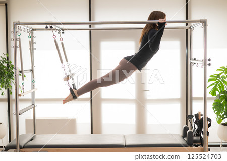 Caucasian woman doing aerial exercises on a reformer machine. Caucasian woman doing aerial exercises on a reformer machine. 125524703