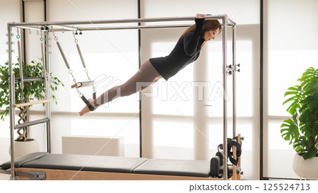 Caucasian woman doing aerial exercises on a reformer machine.  125524713