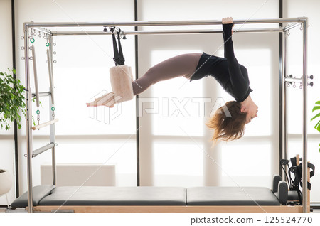 Caucasian woman doing aerial exercises on a reformer machine.  125524770