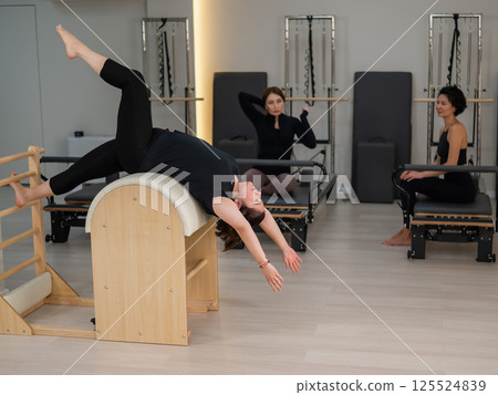 Three women doing Pilates on a reformer and a Pilates barrel.  125524839