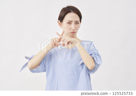Woman, middle-aged, making a "X" gesture with her fingers, white background 125525733