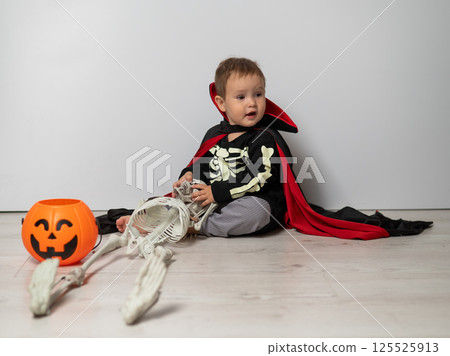 Little Caucasian boy in Dracula costume holding skull on white background. Little Caucasian boy in Dracula costume holding skull on white background. 125525913
