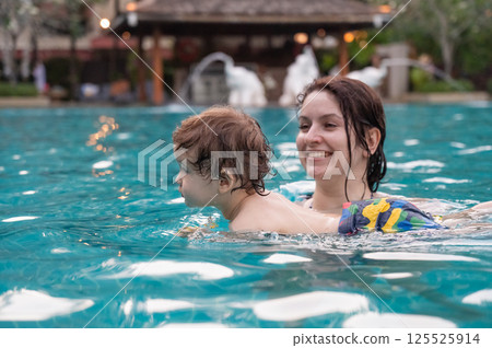 Caucasian woman holds son while swimming in pool on vacation.  125525914