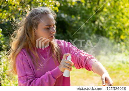 Woman spraying insect repellent at her hand outdoors during summer. Trying to kill mosquitoes and flies. Clearly visible spray droplets. Prevention disinfection against mosquito bite 125526038